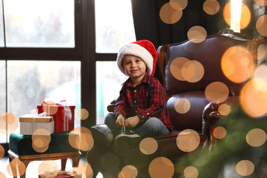 Photo of Little boy in Santa Claus cap near window indoors. Christmas holiday