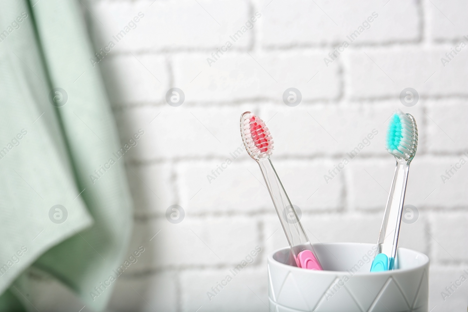 Photo of Cup with toothbrushes against brick wall in bathroom