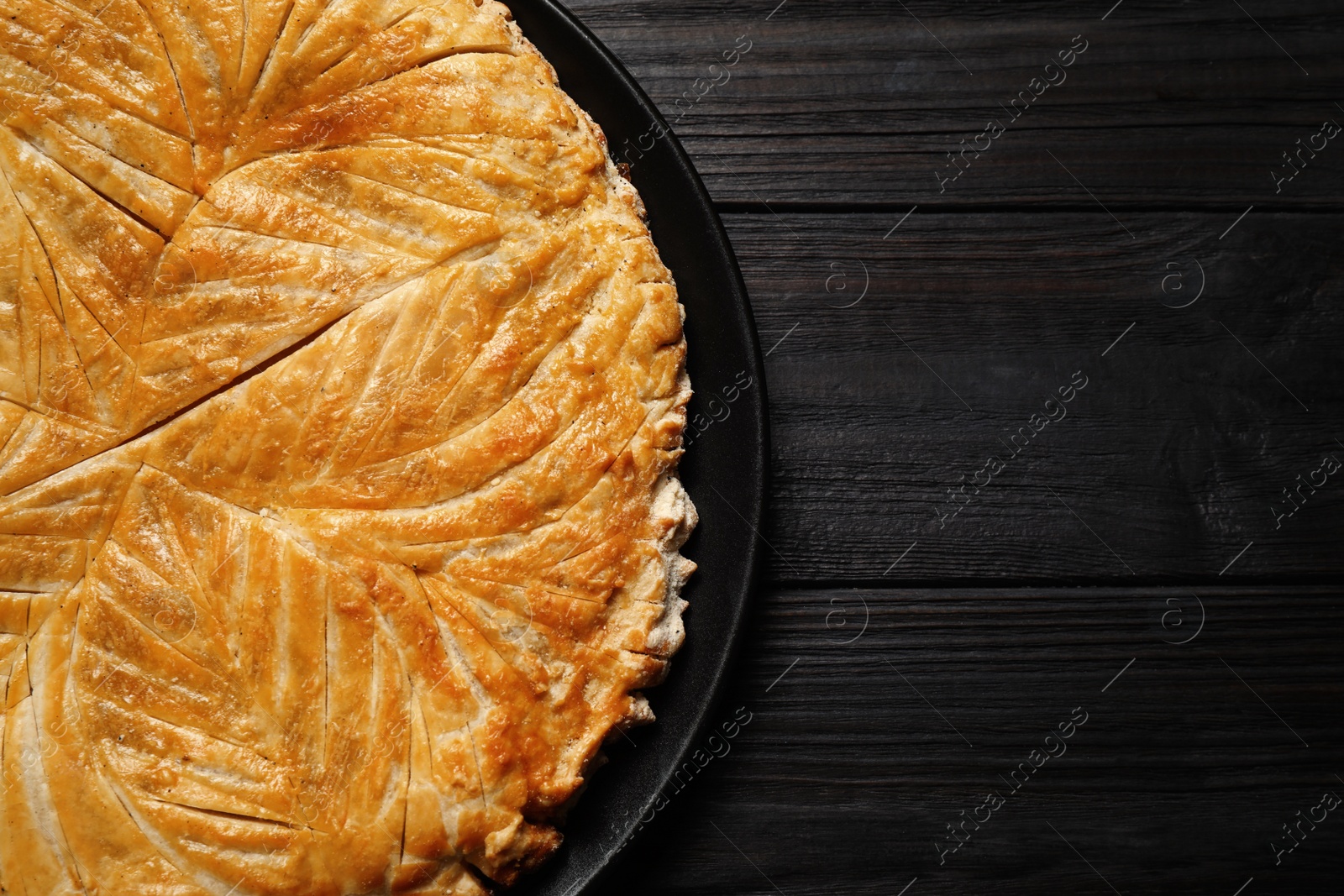 Photo of Traditional galette des rois on black wooden table, top view. Space for text