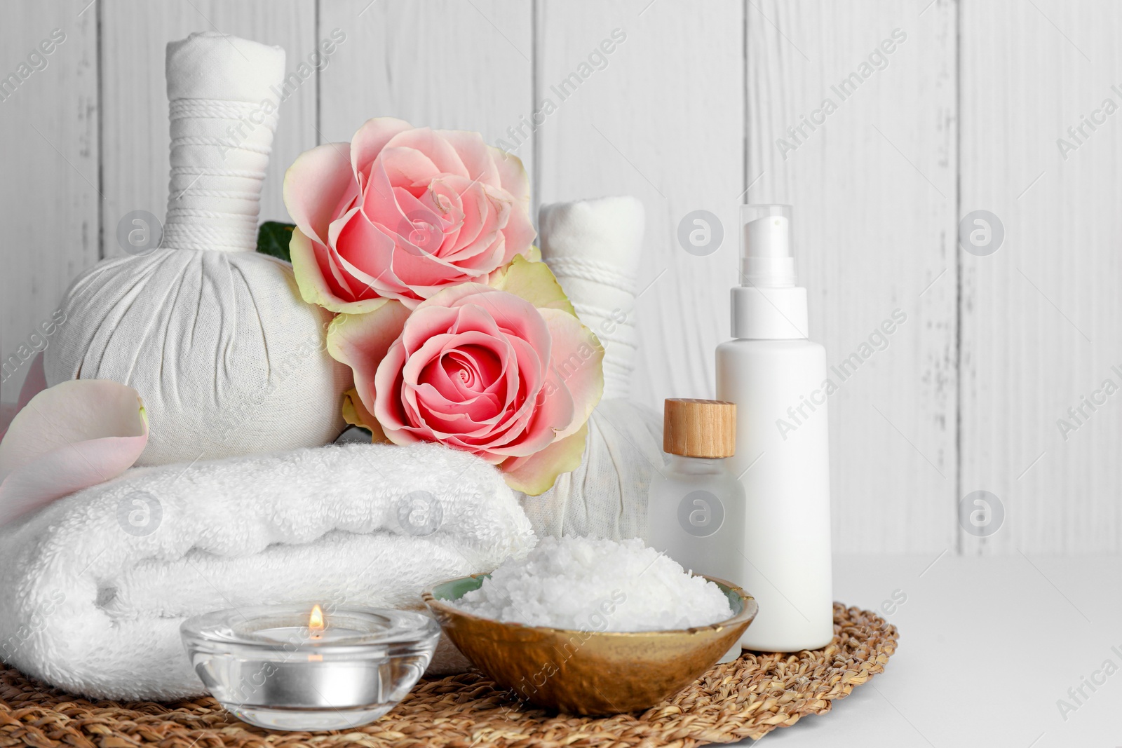 Photo of Composition with different spa products, candle and roses on white table against wooden background