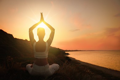 Woman meditating near sea at sunset, back view. Practicing yoga
