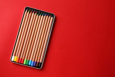 Photo of Box with many colorful pastel pencils on red background, top view and space for text. Drawing supplies
