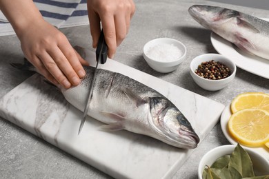 Woman cutting fresh raw sea bass fish at light gray table, closeup