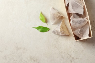Photo of Box with tea bags and leaves on grey table, flat lay. Space for text