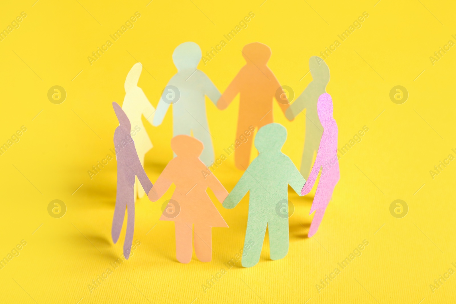 Photo of Many different paper human figures standing in circle on yellow background. Diversity and inclusion concept