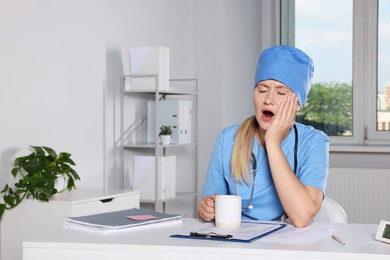 Photo of Tired young doctor yawning at workplace in office