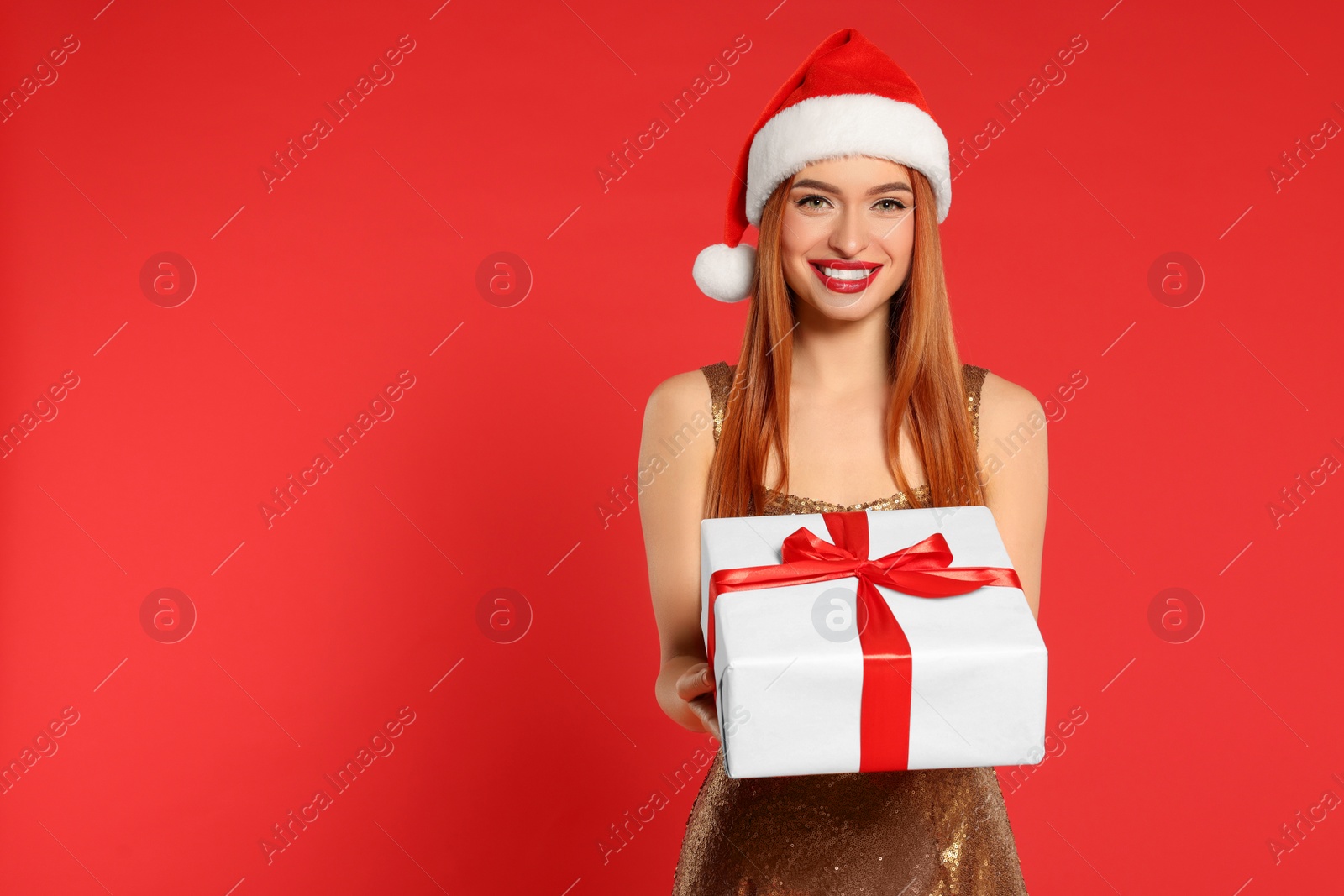 Photo of Young woman in Santa hat with Christmas gift on red background, space for text