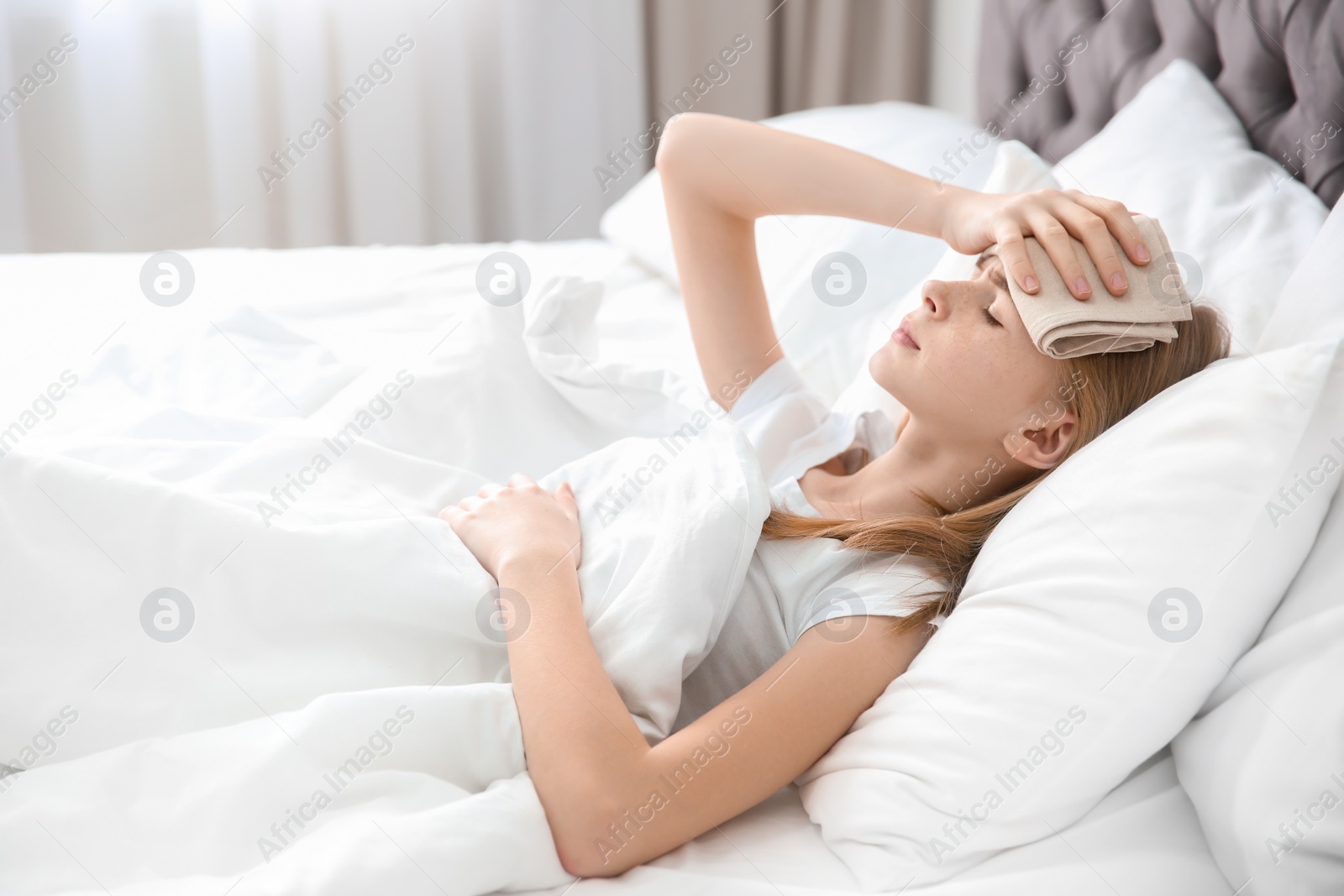 Photo of Teenage girl suffering from headache while lying in bed at home