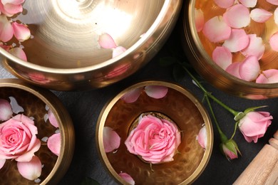 Photo of Tibetan singing bowls with water and beautiful rose flowers on table, flat lay