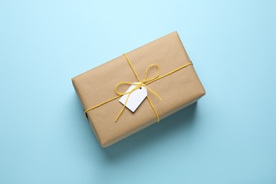 Photo of Parcel wrapped in kraft paper with tag on light blue background, top view