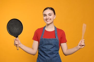 Photo of Beautiful young woman in clean denim apron with kitchen tools on orange background