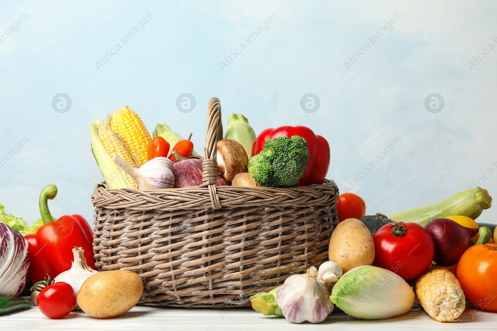 Photo of Fresh vegetables and wicker basket on white wooden table