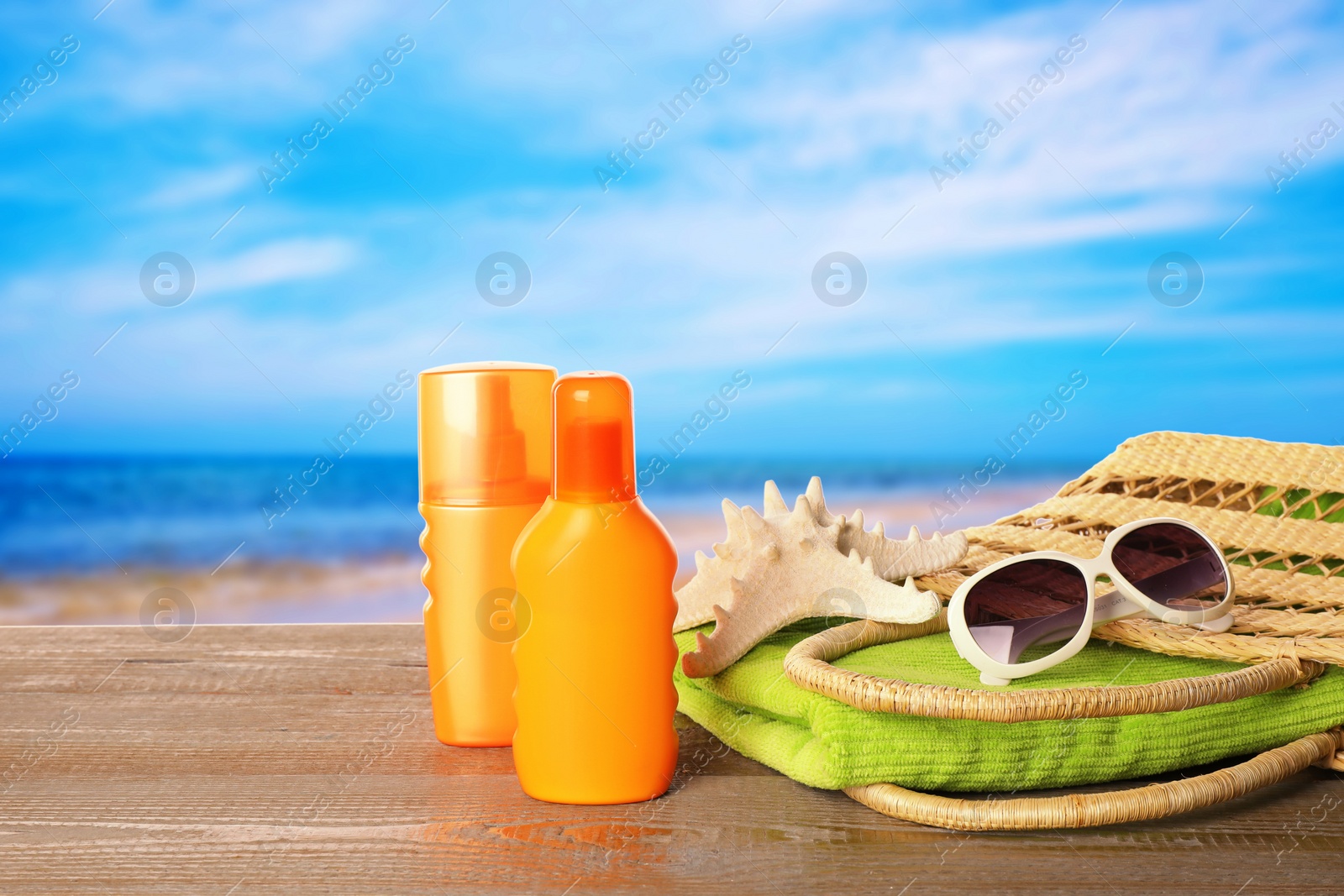 Image of Set of sun protection products and stylish accessories on wooden table near sea