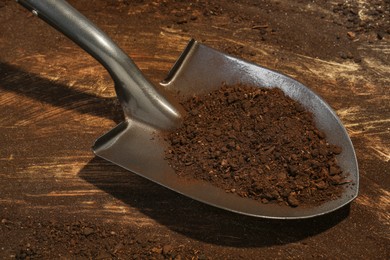 Metal shovel with fertile soil on dirty wooden surface