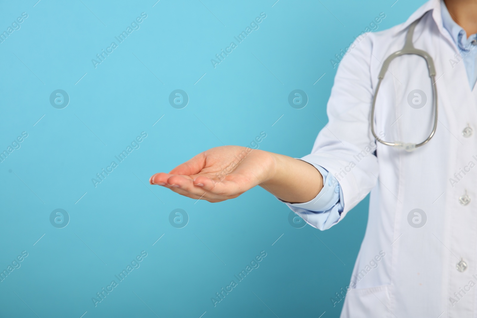 Photo of Doctor with stethoscope holding something on light blue background, closeup. Space for text