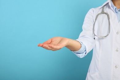 Doctor with stethoscope holding something on light blue background, closeup. Space for text