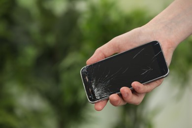 Woman holding damaged smartphone on blurred green background, closeup with space for text. Device repairing