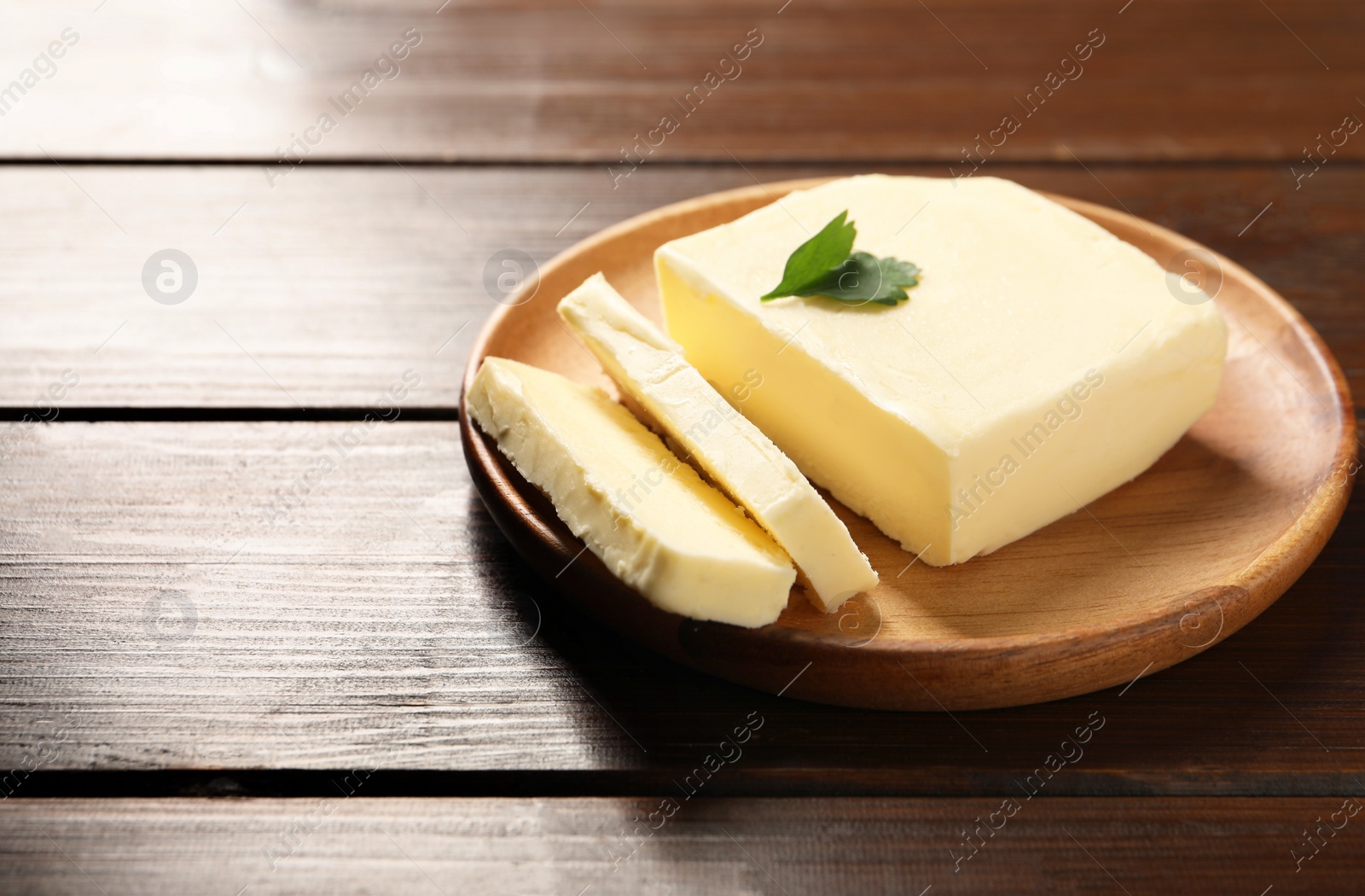 Photo of Cut tasty butter with parsley on wooden table