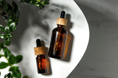 Photo of Glass bottles of essential oil and green plant on white table, flat lay. Space for text