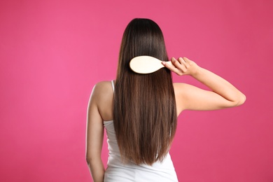 Back view of young woman with hair brush on color background