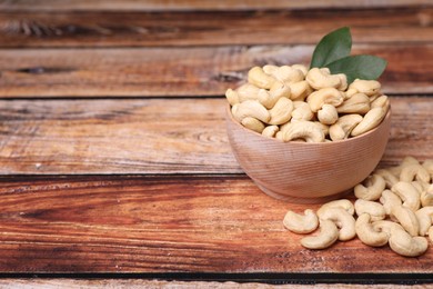 Photo of Tasty cashew nuts and green leaves on wooden table, space for text