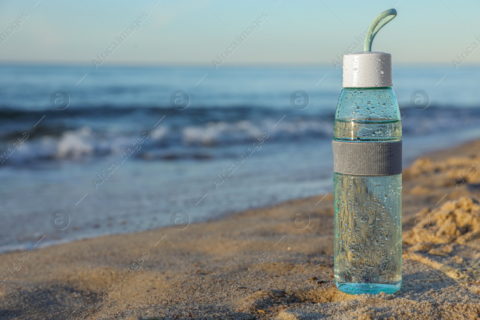 Photo of Glass bottle with water on wet sand near sea. Space for text