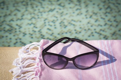 Stylish sunglasses and blanket near outdoor pool on sunny day, space for text