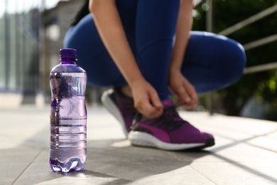 Plastic bottle of pure water and athletic woman outdoors, closeup