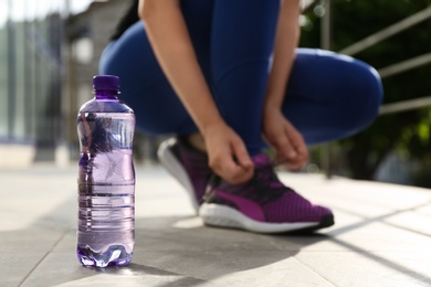 Photo of Plastic bottle of pure water and athletic woman outdoors, closeup