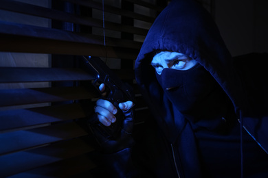 Photo of Man in mask with gun near window indoors. Dangerous criminal