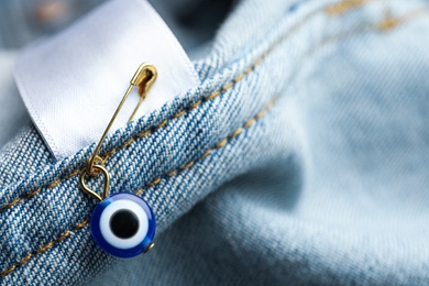 Photo of Evil eye safety pin on denim clothing, closeup
