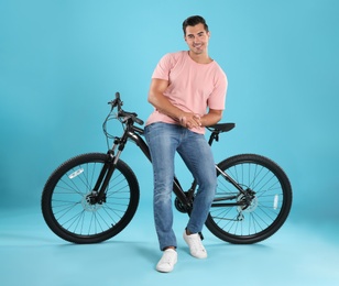 Handsome young man with modern bicycle on light blue background