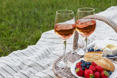 Glasses of delicious rose wine, food and basket on picnic blanket outdoors