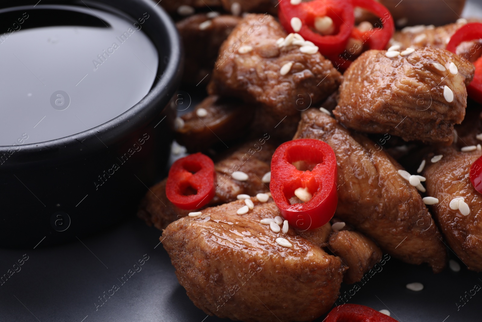 Photo of Tasty soy sauce, roasted meat with chili pepper and sesame on dark plate, closeup