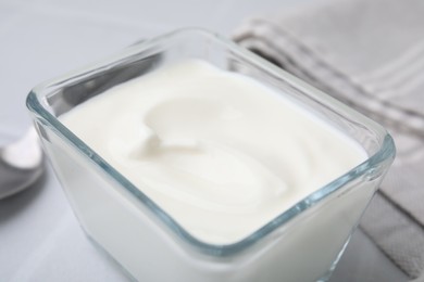 Delicious natural yogurt in glass bowl on white table, closeup