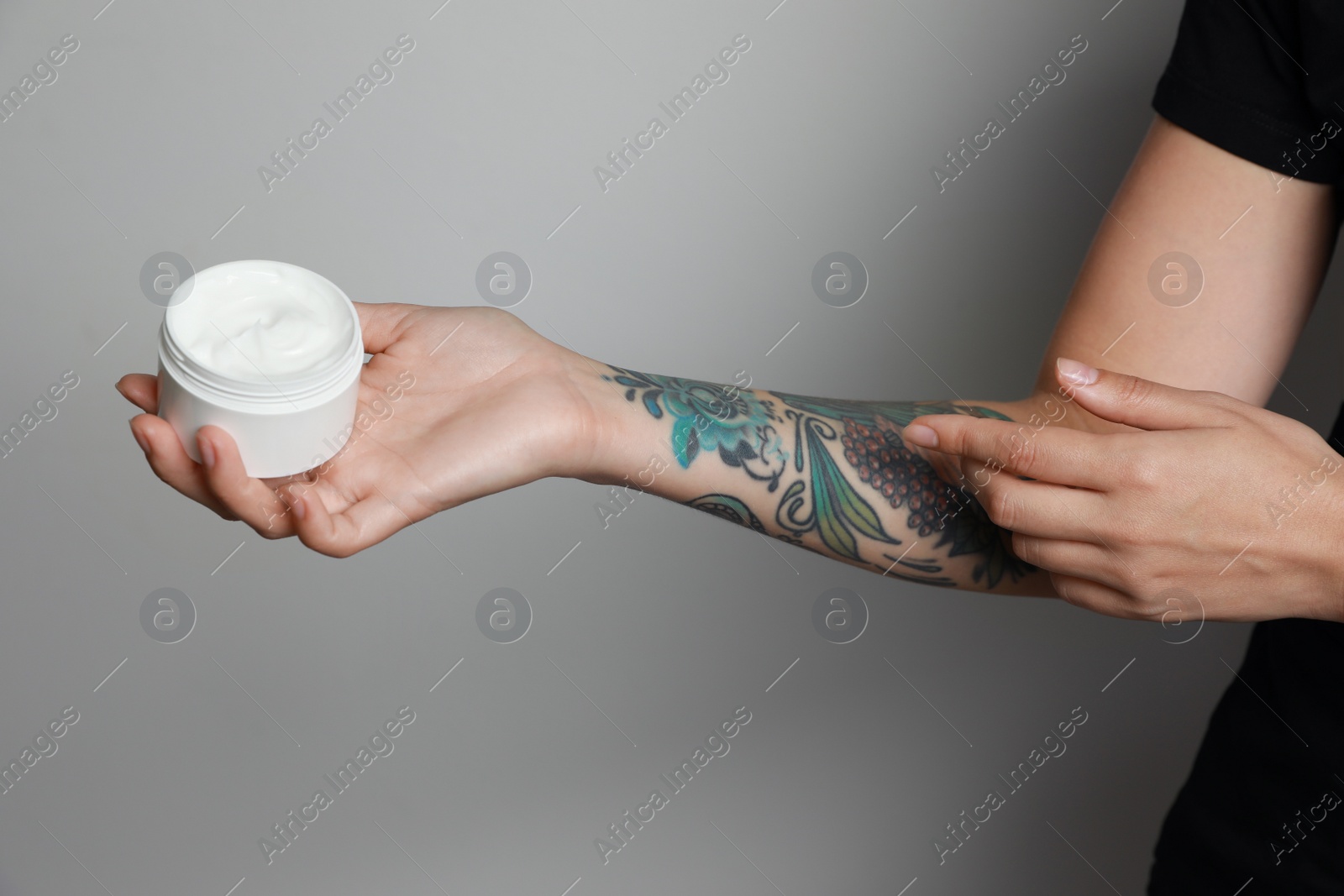 Photo of Woman applying cream on her arm with tattoos against light grey background, closeup