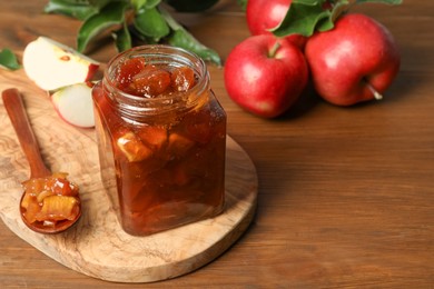 Tasty apple jam in glass jar and fresh fruits on wooden table, space for text