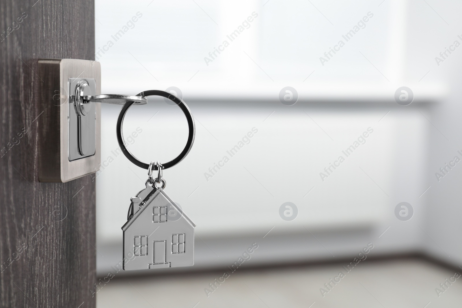 Photo of Mortgage and real estate. Open door with key and house shaped keychain against blurred background, space for text