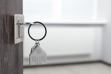 Photo of Mortgage and real estate. Open door with key and house shaped keychain against blurred background, space for text