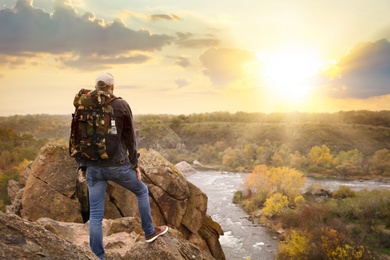 Hiker with travel backpack enjoying beautiful view near mountain river, back view