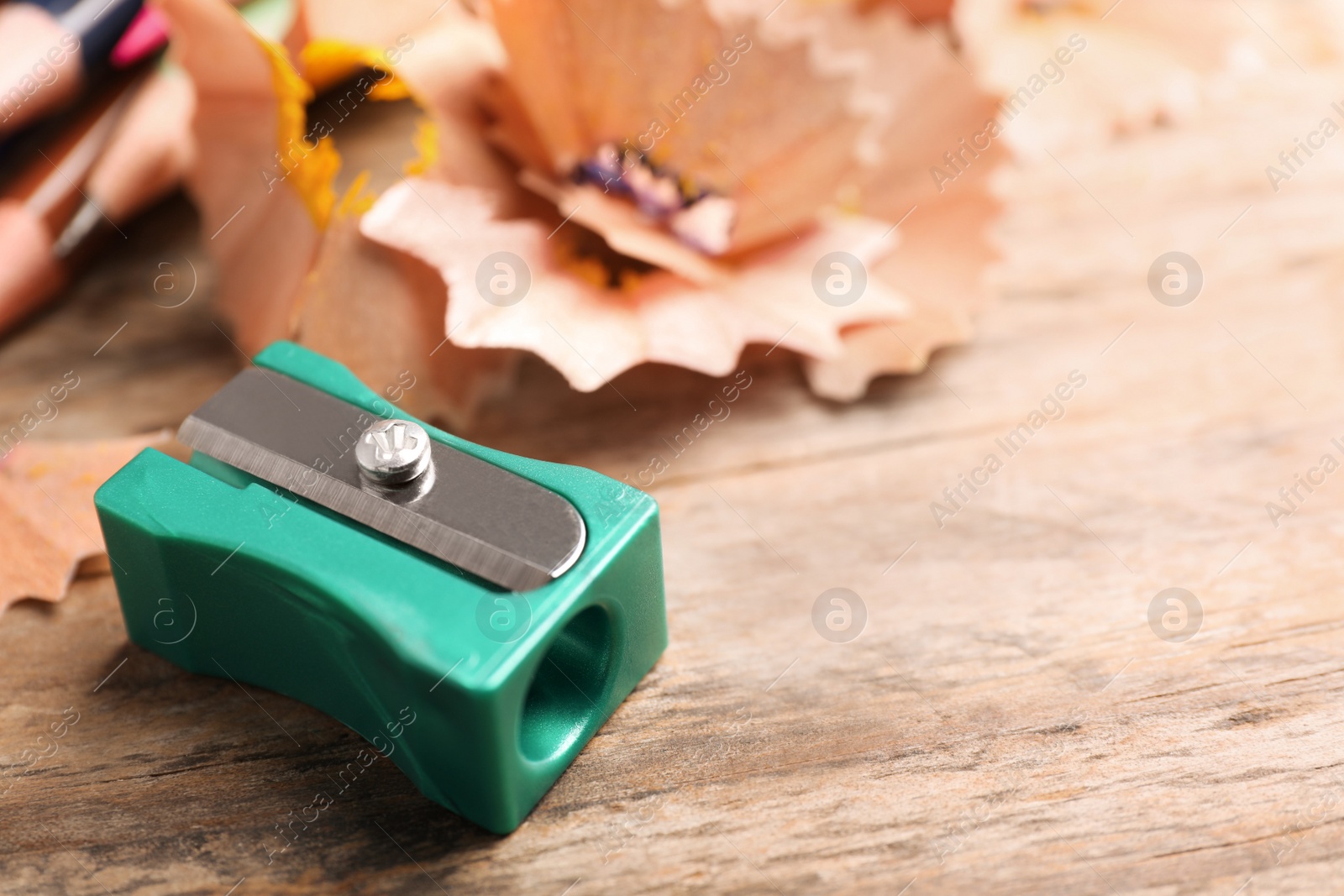 Photo of Turquoise sharpener and pencil shavings on wooden table, closeup. Space for text