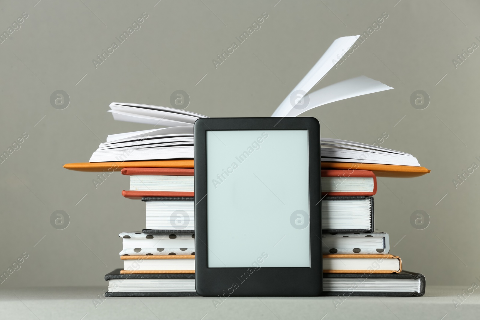 Photo of Modern e-book reader and stack of hard cover books on light grey table