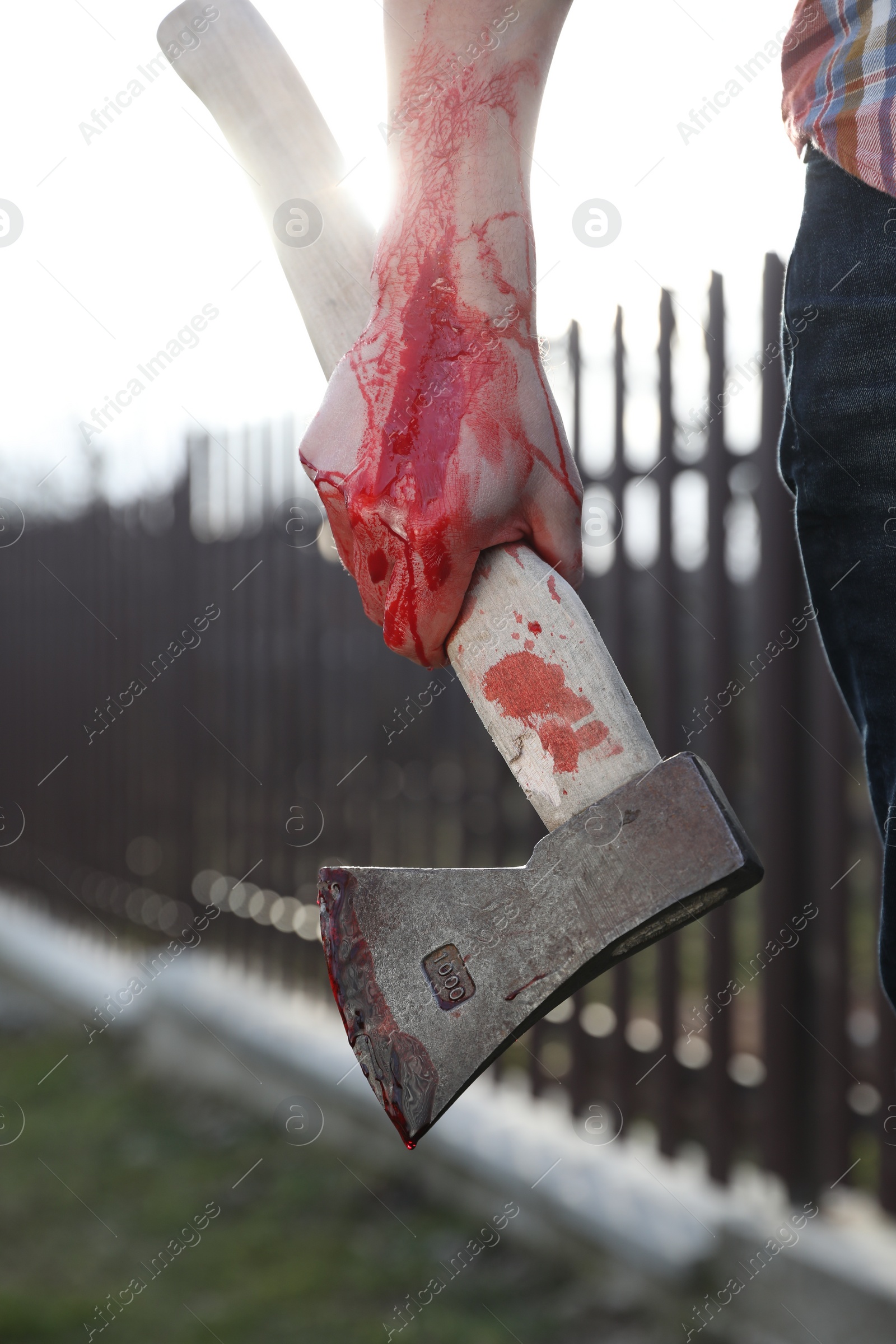 Photo of Man holding bloody axe outdoors, closeup view