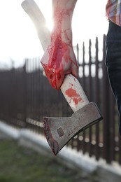 Man holding bloody axe outdoors, closeup view