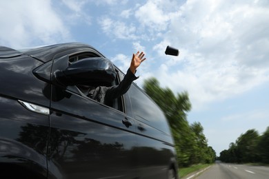 Photo of Driver throwing away paper coffee cup from car window, low angle view. Garbage on road