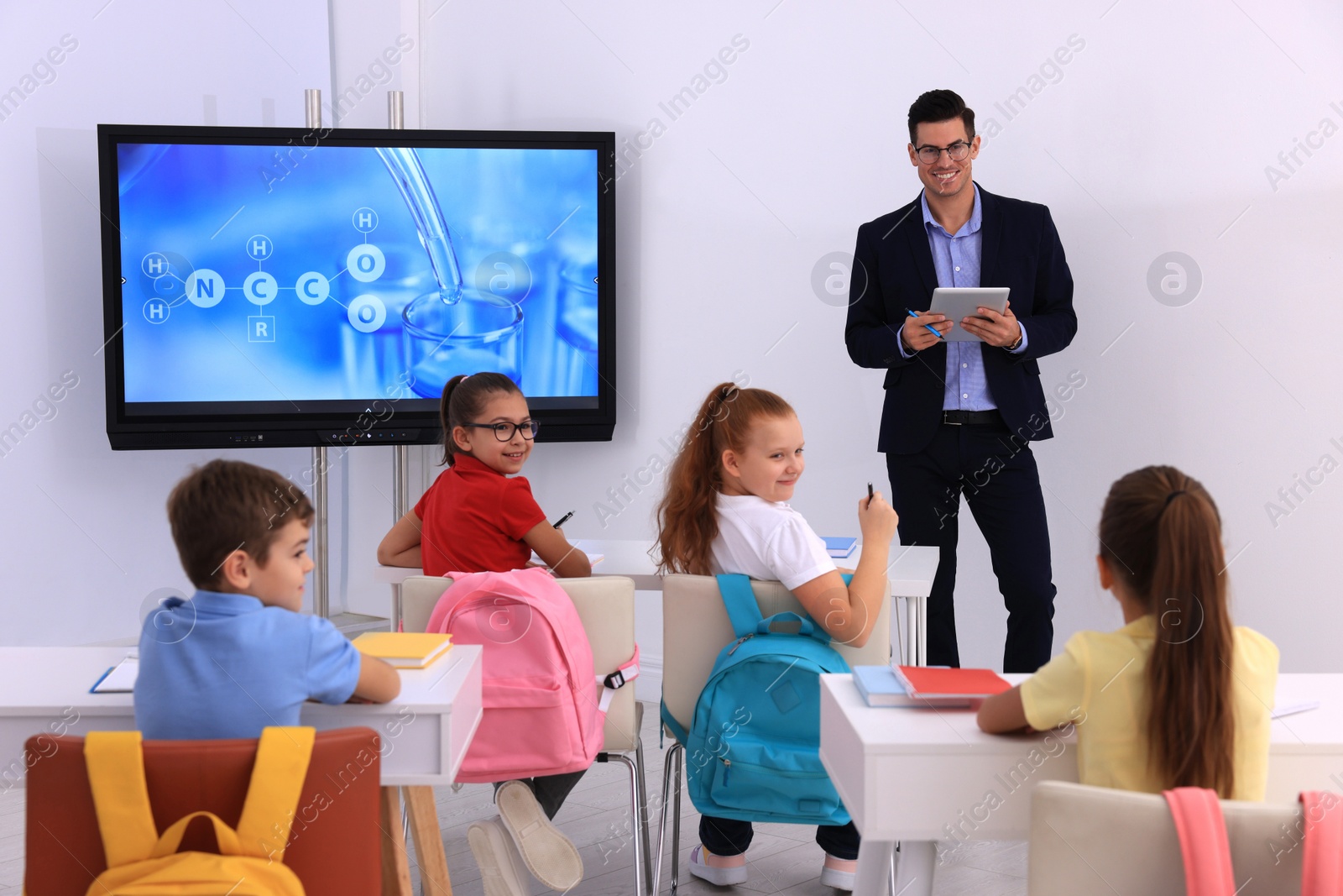 Photo of Teacher giving lesson to pupils near interactive board in classroom