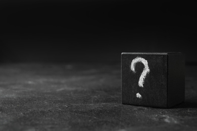 Wooden cube with question mark on black stone table. Space for text