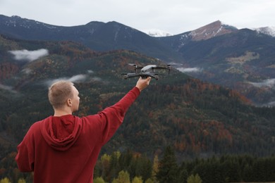 Young man with modern drone in mountains, back view