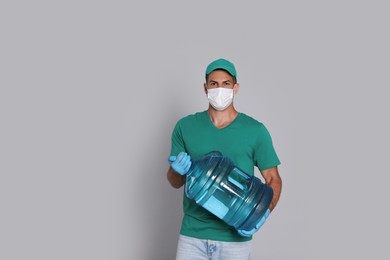 Courier in medical mask holding bottle for water cooler on light grey background. Delivery during coronavirus quarantine