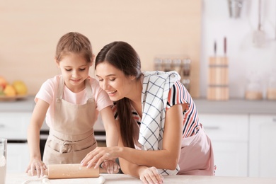 Mother and her daughter preparing dough at table in kitchen